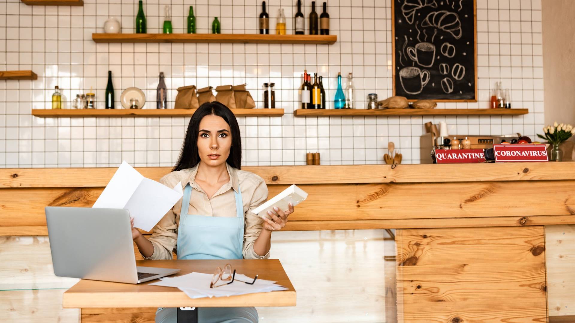 Eine Café-Besitzerin sitzt überfordert an einem Tisch und kümmert sich um die Finanzen.