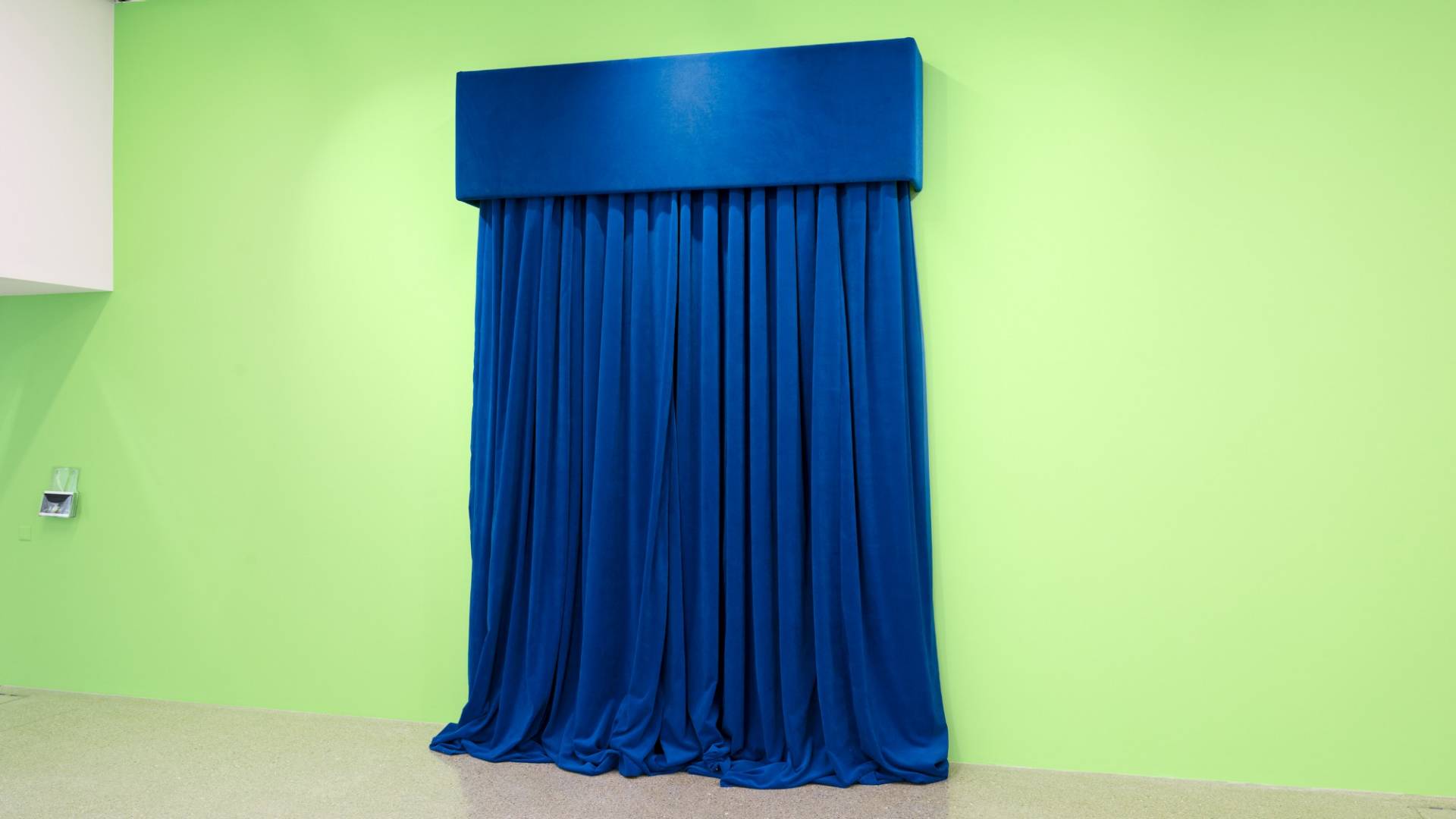 Blauer, schwer wirkender Samtvorhang vor grün gestrichener Wand.