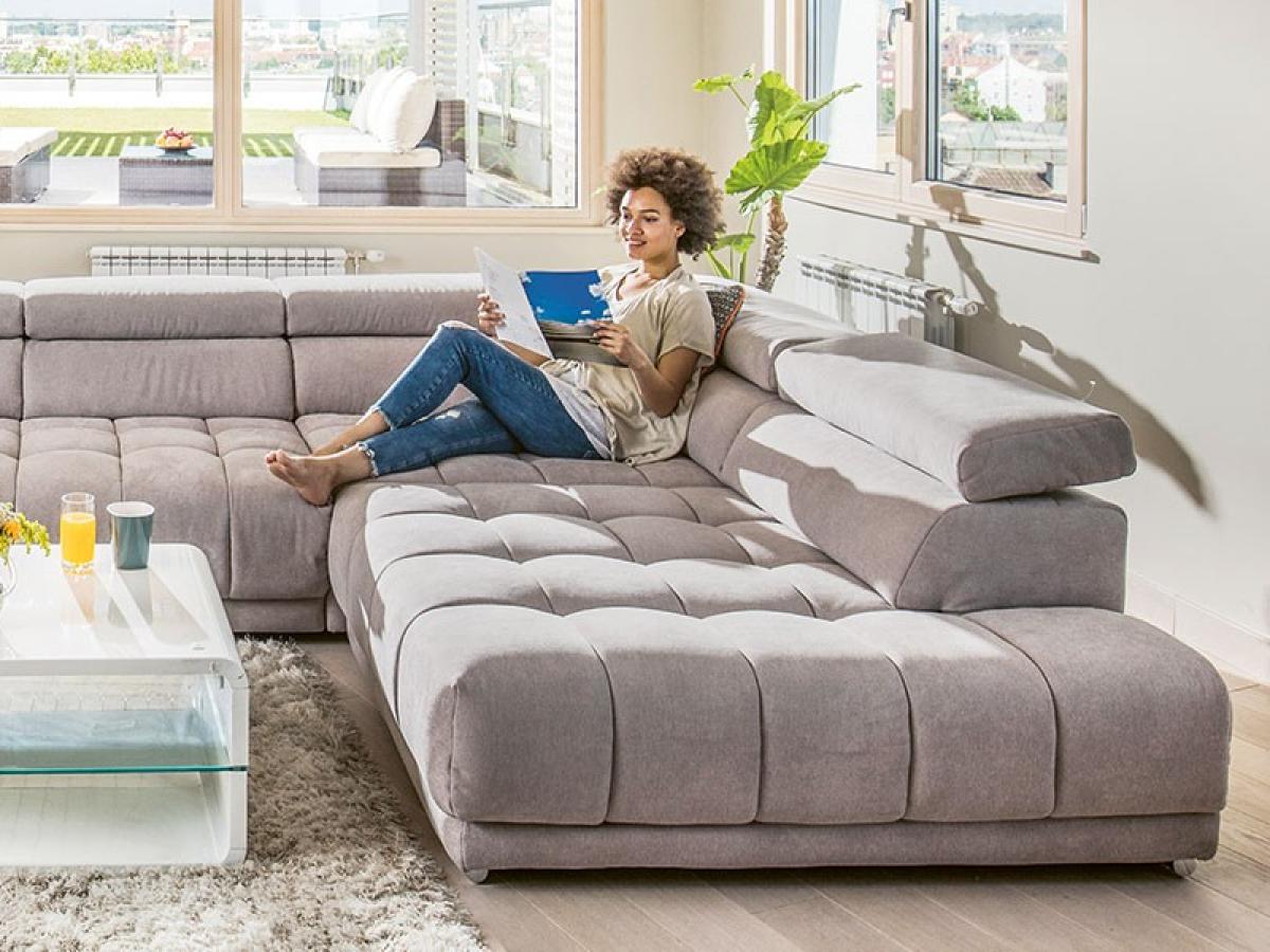 Eine Frau sitzt auf einer grauen Couch und hält ein Prospekt in der Hand.