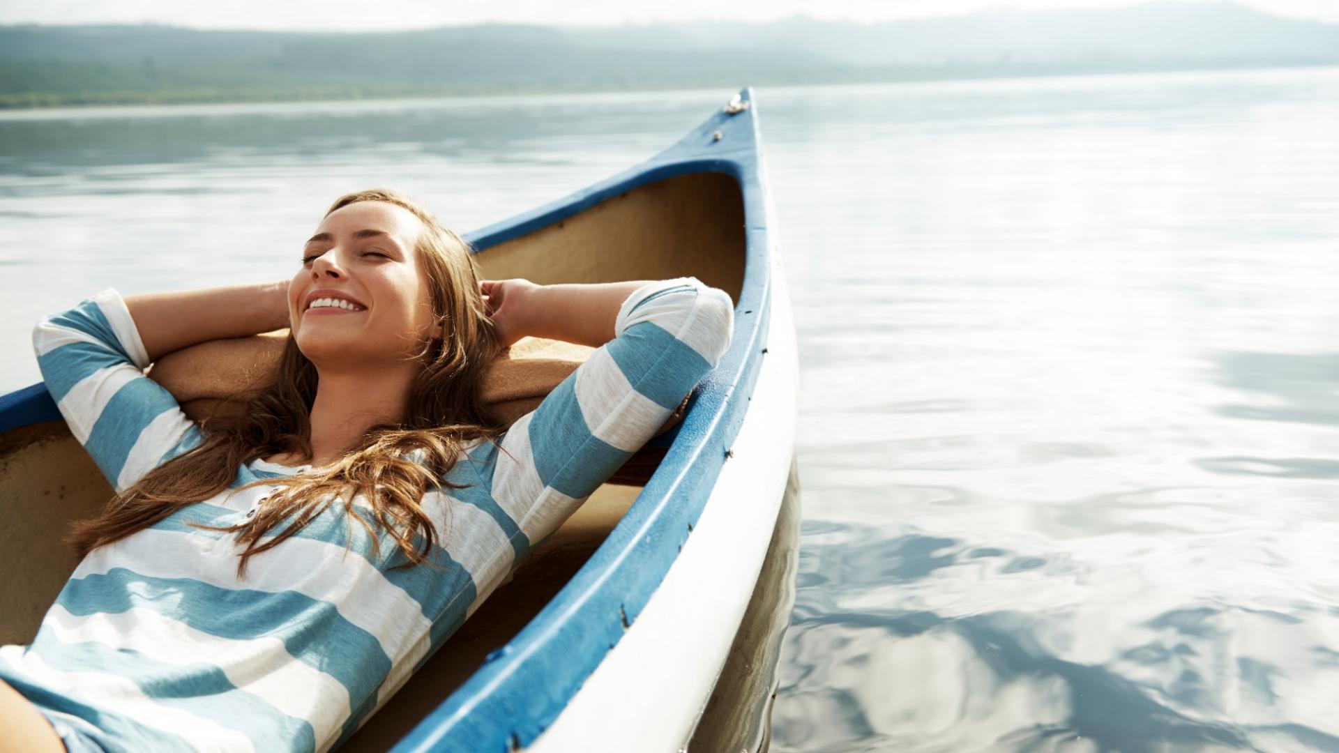 Eine junge Frau liegt entspannt in einem Boot, das auf einem See schwimmt.
