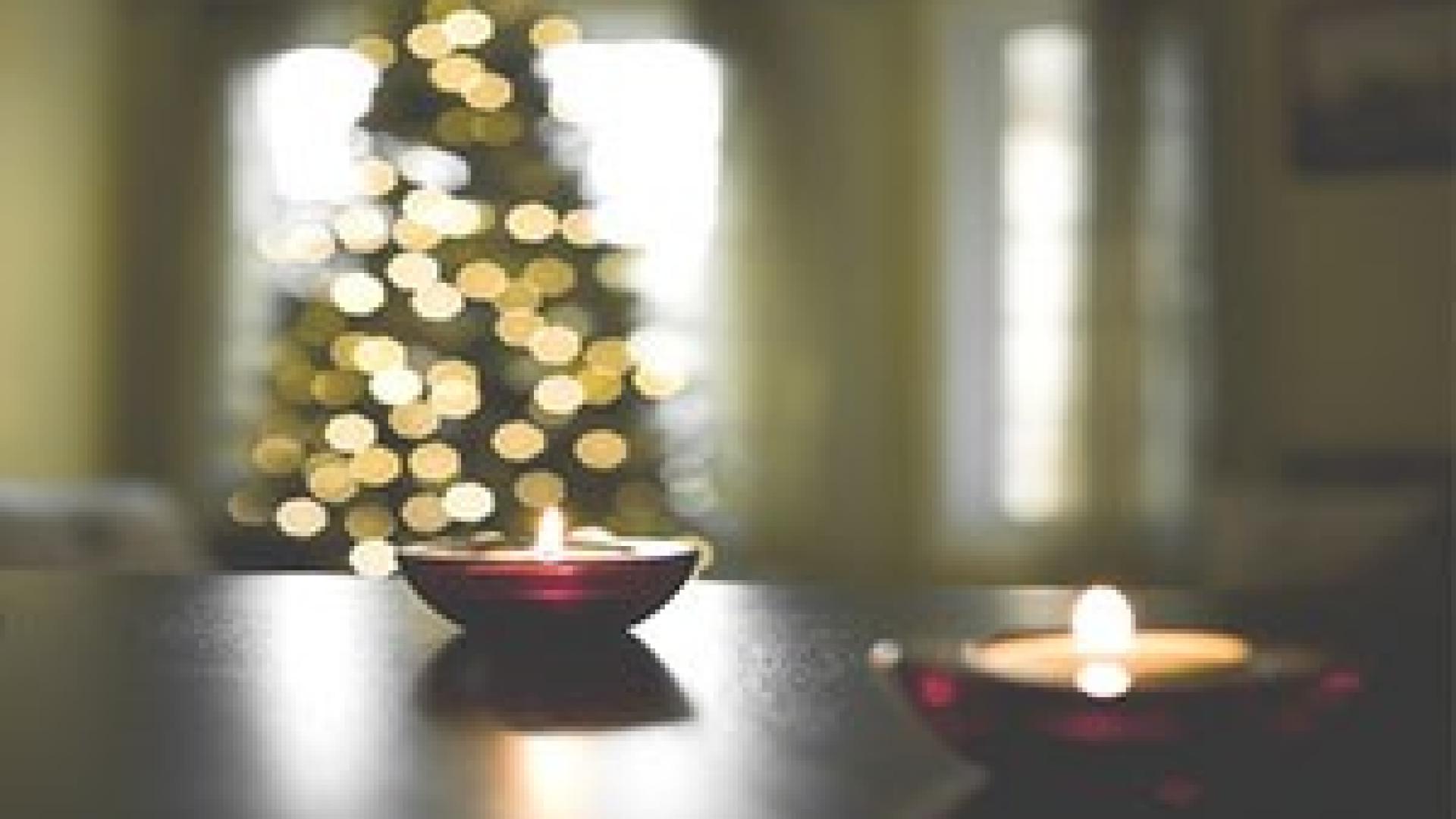 Brennende Teelichte stehen vor einem Weihnachtsbaum auf dem Tisch.