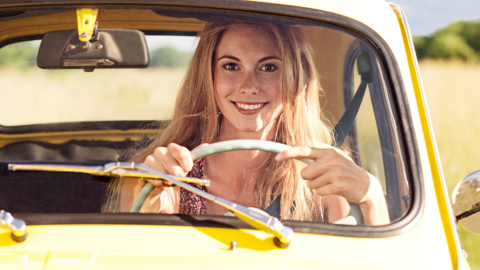 Eine junge Frau sitzt lächelnd in einem gelben Auto.