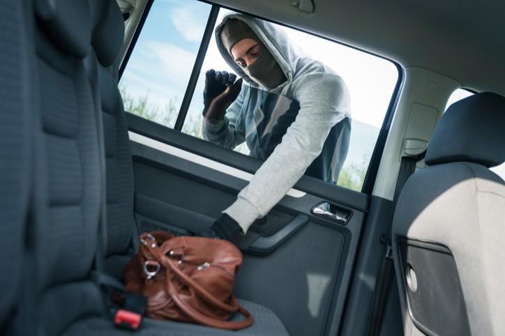 Ein maskierter Mann greift eine Handtasche durch ein Auto-Fenster