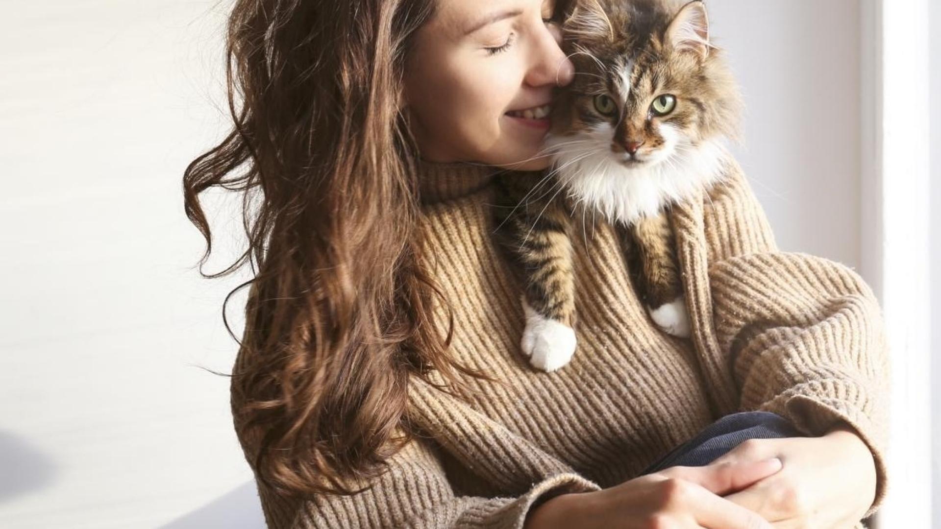 Auf dem Bild ist eine glückliche Katzenbesitzerin zu sehen, die ihre Katze auf der Schulter hat.