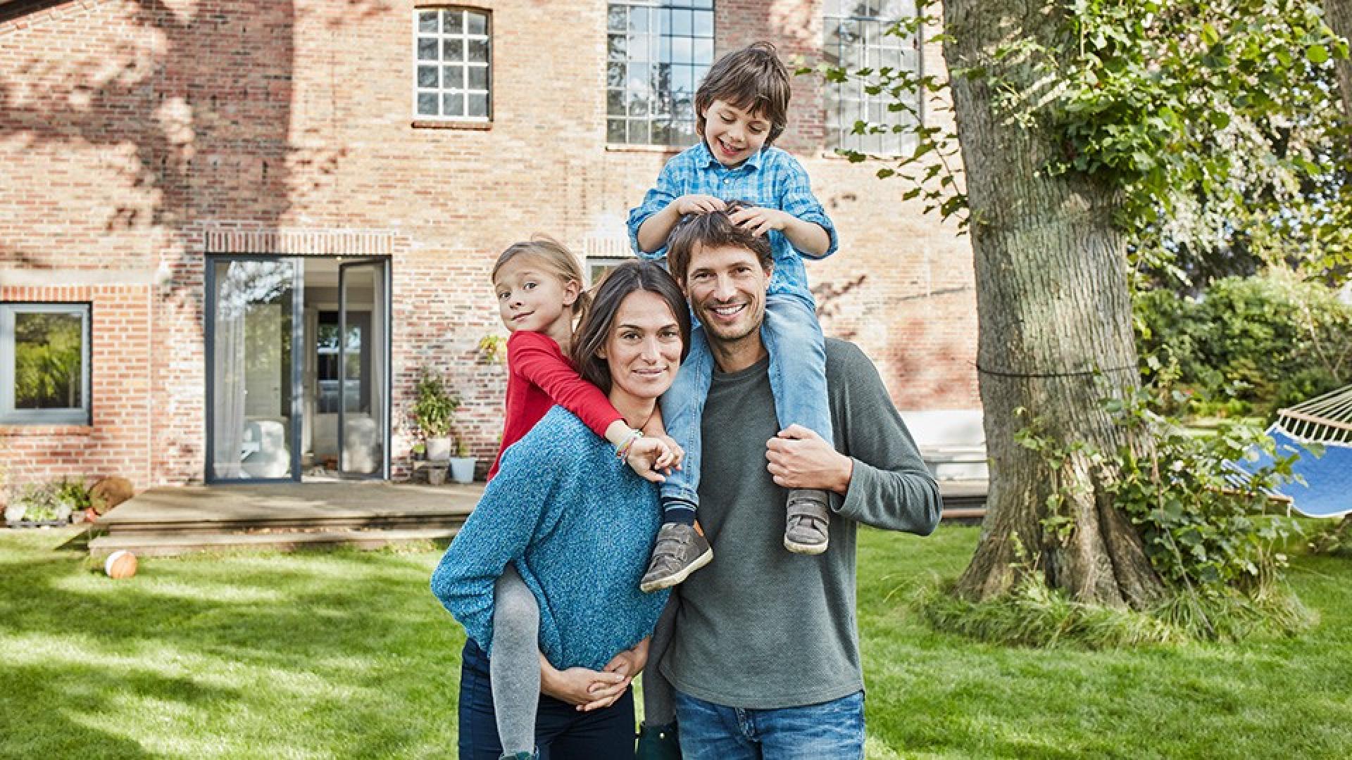 Eine glückliche Familie vor ihrem Haus - Wohngebäudeversicherung